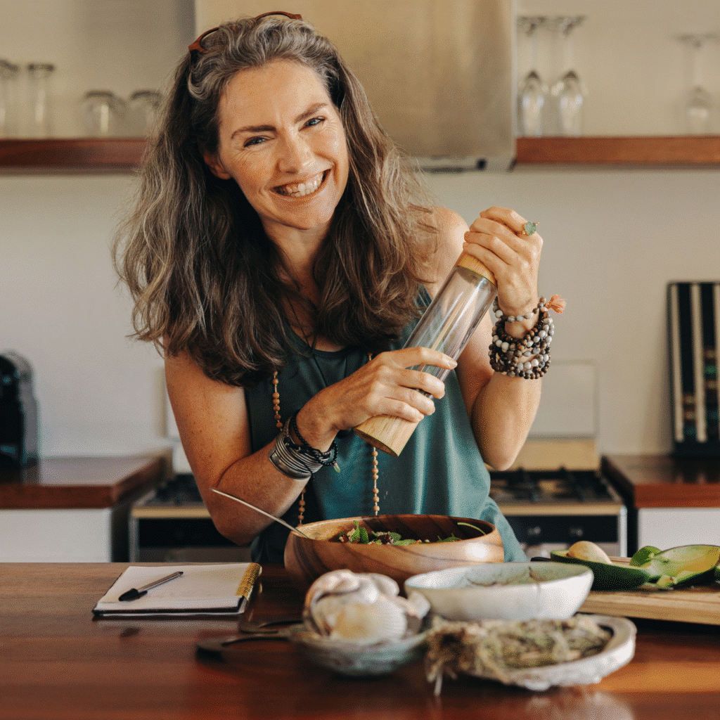 About 2 Olivia Bennett writing down new recipe ideas at her kitchen table, surrounded by fresh produce